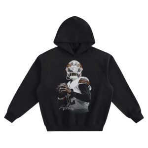 Shedeur Sanders Big Face Hoodie graphic showing Shedeur Sanders in a helmet with visor holding a football, with a script signature detail on a black hoodie.