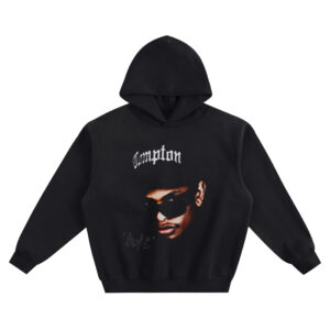 Eazy-E Big Face Hoodie graphic showing Eazy-E in sunglasses and a black cap with “Compton” text above and a small signature-style mark on a black hoodie.